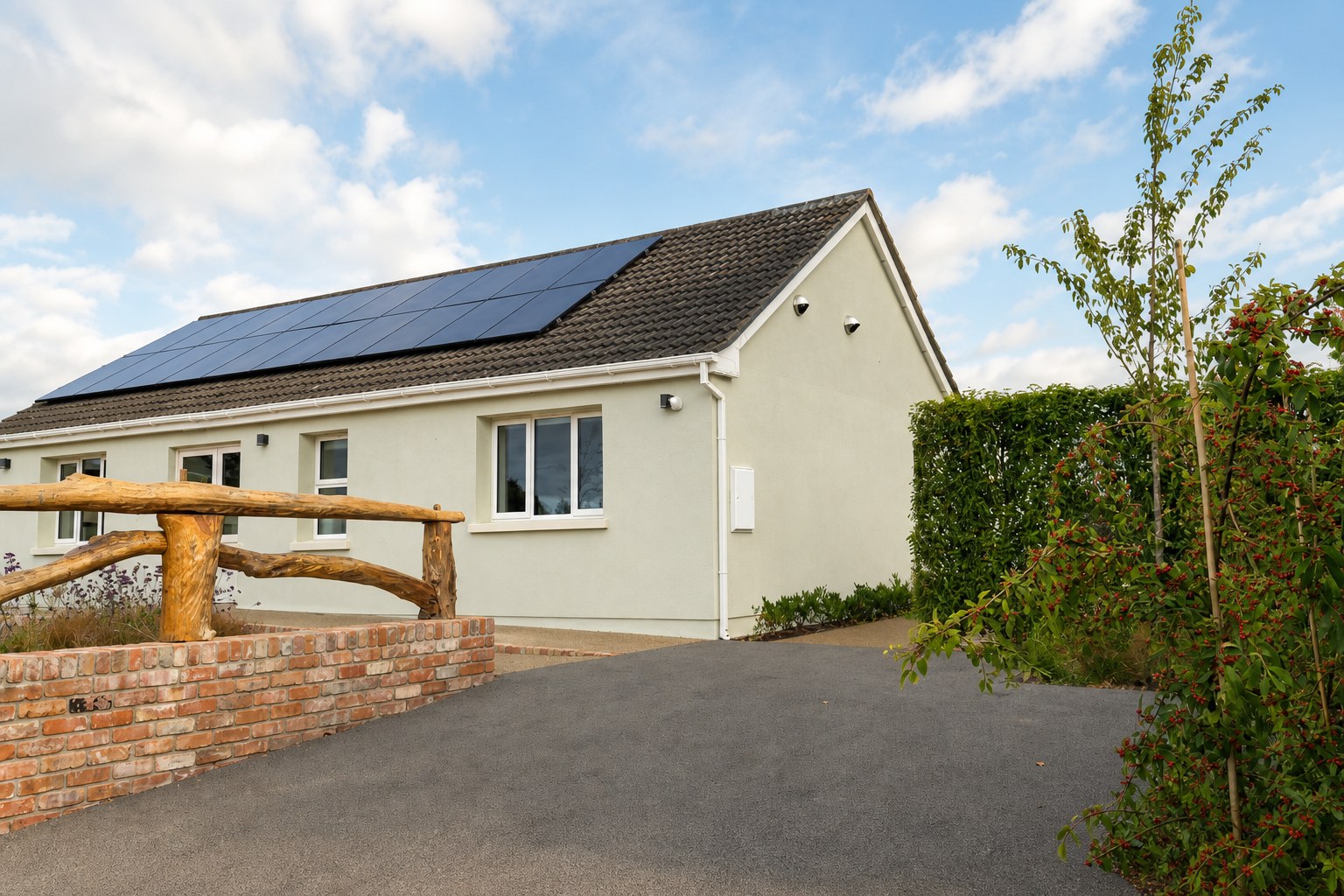 Drive and sage exterior of Heron House, with solar roof and a rustic log fence