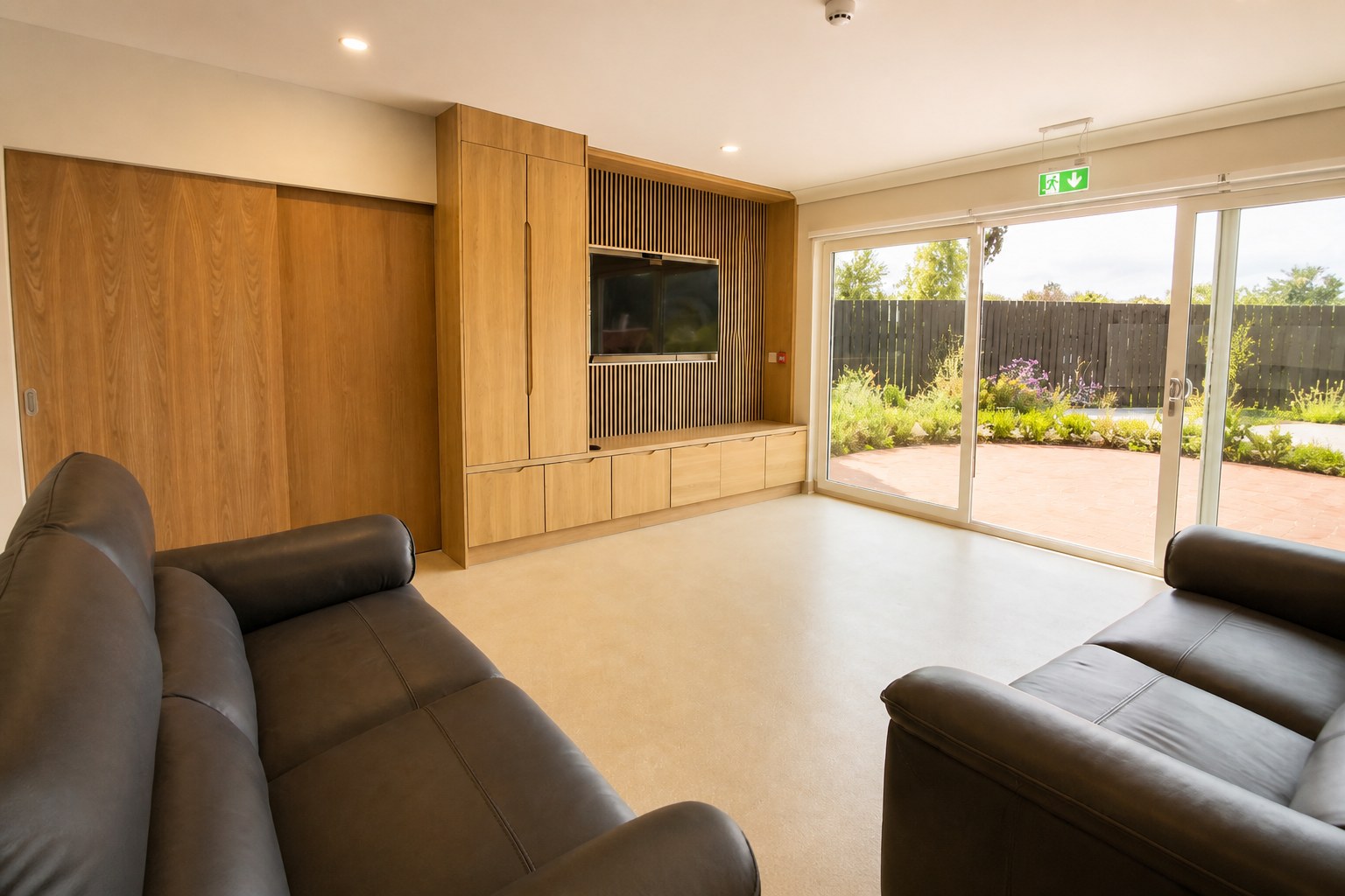 Shared living room at Heron House with grey sofas, an oak media wall, and garden doors